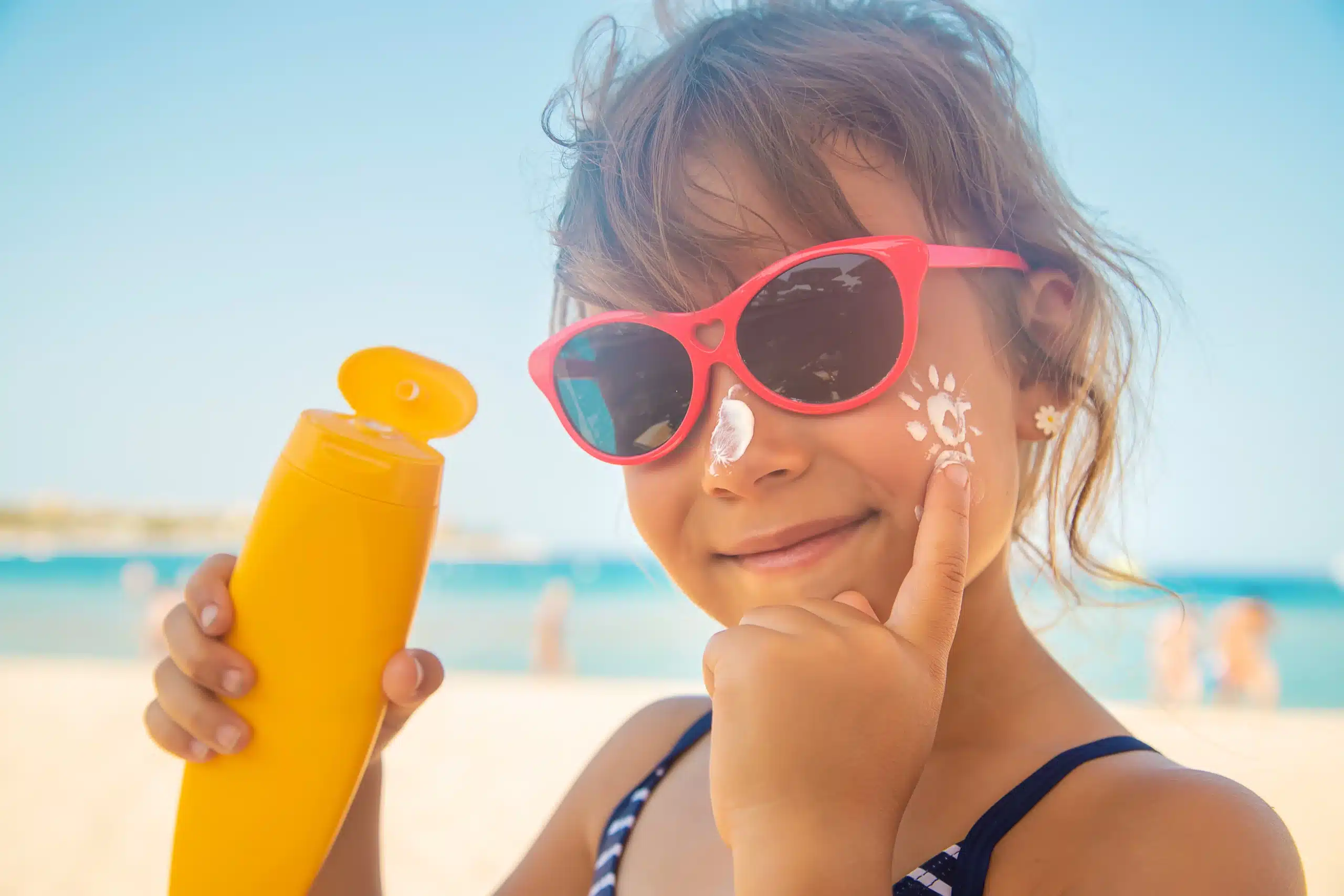 Dziewczynka na plaży, która smaruje się kremem do opalania po twarzy.